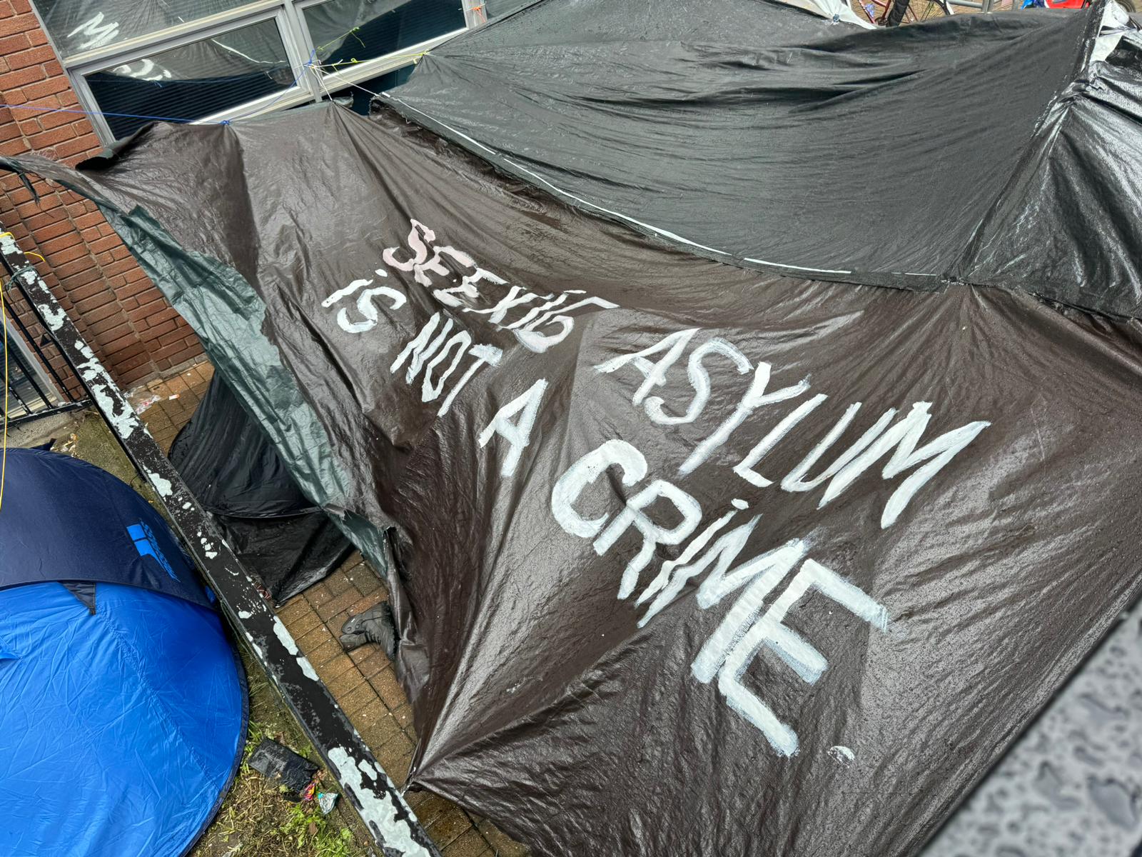 Las tiendas de campaña están cubiertas de mensajes de graffiti que dicen “buscar asilo no es un crimen”